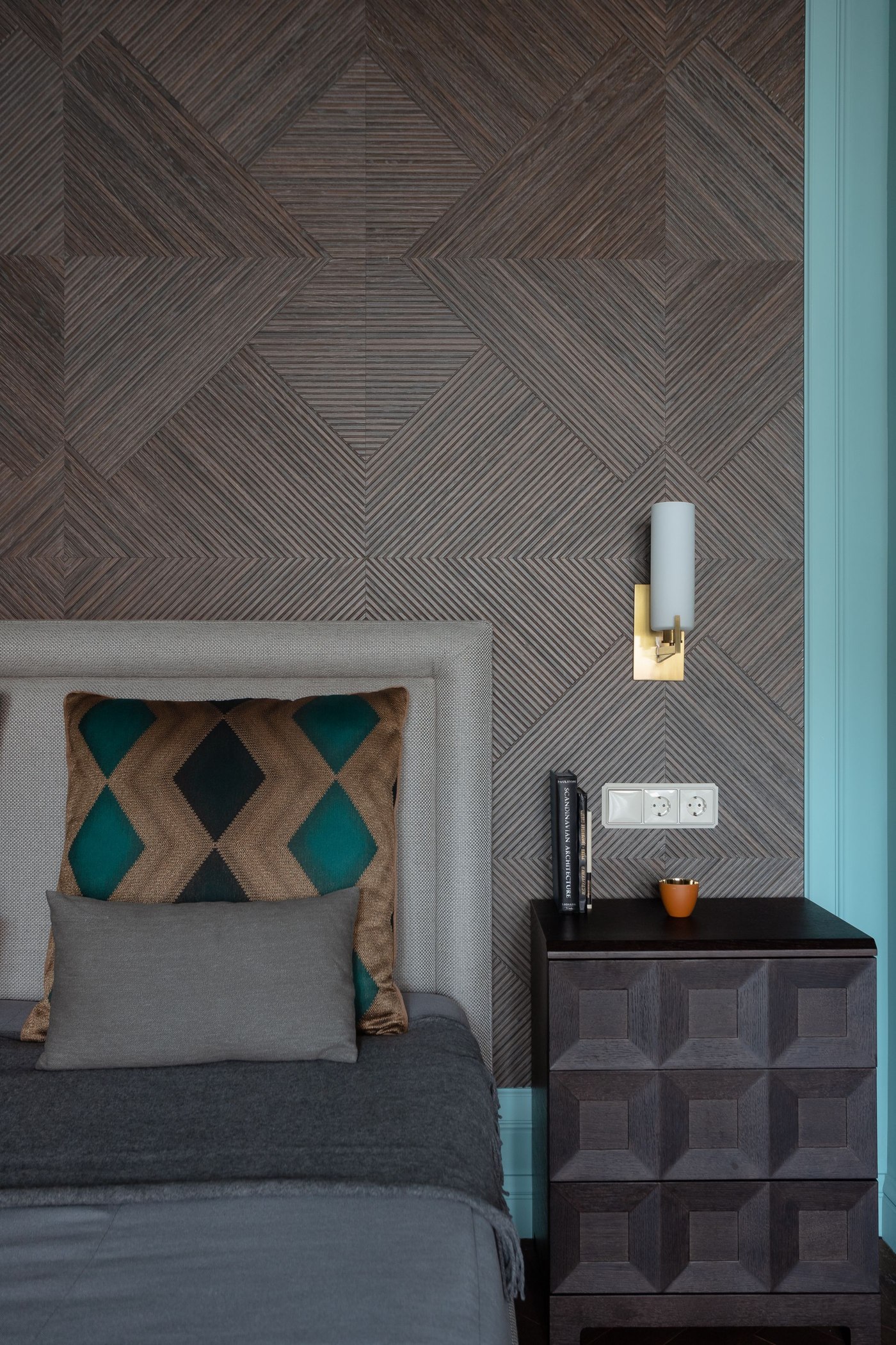 Textured repeating geometric wallpaper behind a gray bed and side table